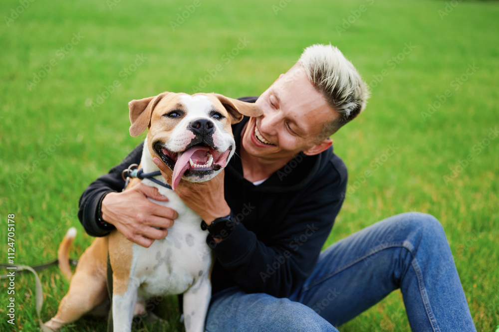 A dog and a man are sitting on the grass and smiling, the dog has his tongue out. Man hugging dog in park. The concept of human to animal friendship. A dog and a man are sitting on the grass and smiling, the dog has his tongue out. Man hugging dog in park. The concept of human to animal friendship.