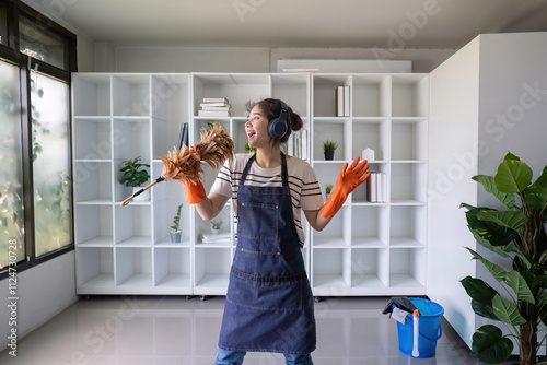 Happy young Asian woman dancing and singing with a feather duster while cleaning photo