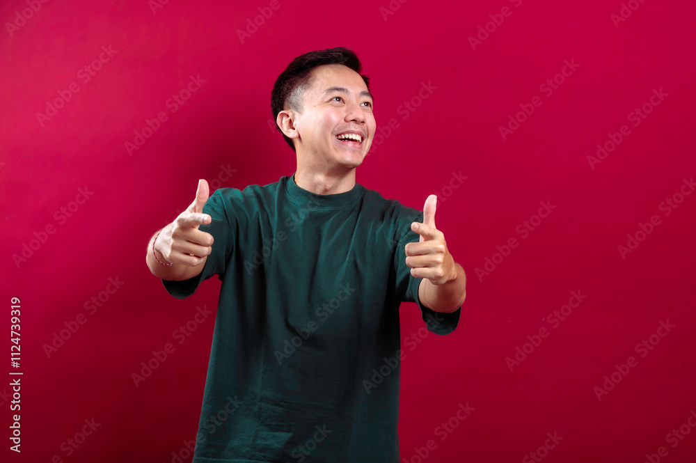 An Asian man in a green t-shirt smiles brightly, pointing directly at the camera with both hands, exuding positivity and engagement against a vivid red background, emphasizing confidence An Asian man in a green t-shirt smiles brightly, pointing directly at the camera with both hands, exuding positivity and engagement against a vivid red background, emphasizing confidence