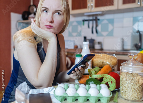 A woman checks the calorie content of food in a smartphone app. Calorie counting for weight loss. There are products for dieting on the table