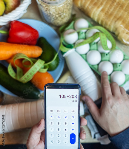 A man checks the calorie content of food products in a smartphone app. Calorie calculator for weight loss. On the table are products for consumption during a diet