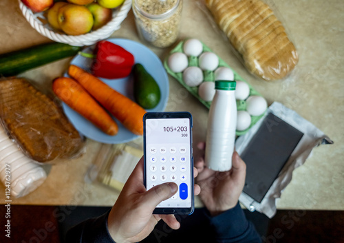 A man checks the calorie content of food products in a smartphone app. Calorie calculator for weight loss. On the table are products for consumption during a diet