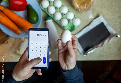 A man checks the calorie content of food products in a smartphone app. Calorie calculator for weight loss. On the table are products for consumption during a diet