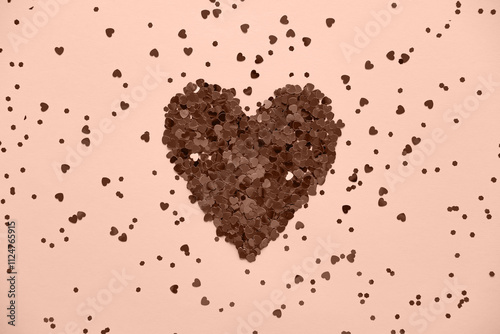 Heart made of shiny red small decorative hearts on a pink background strewn with sparkles. Flat lay, place for text. Festive minimal composition. Color of the Year Mocha Mousse.