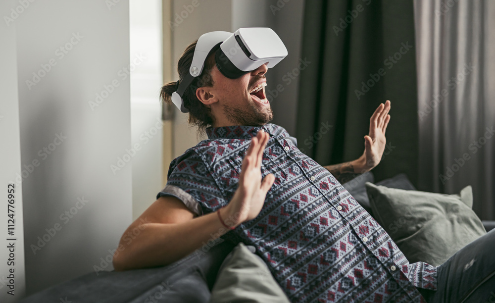 Man wearing VR headset, fully immersed and enjoying a virtual reality experience while sitting on a couch at home. Man wearing VR headset, fully immersed and enjoying a virtual reality experience while sitting on a couch at home.