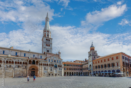Obraz na płótnie Visitors stroll through the vibrant Piazza Grande in Modena, surrounded by stunning historic buildings and a bright blue sky. w salonie