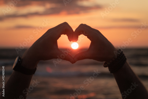 silhouette of hands and fingers forming heart in the sunset over ocean