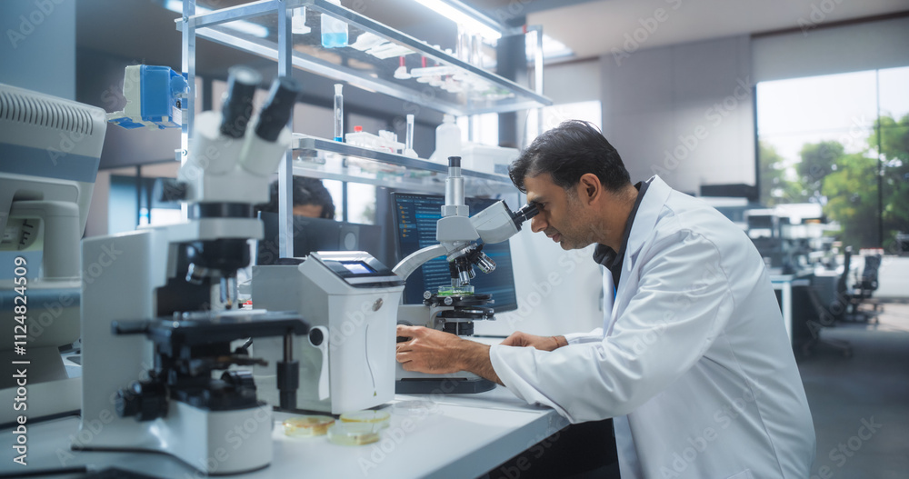 Genetic Research and Development Laboratory: Adult Scientist Working on a Computer and Looking at a Sample in a Petri Dish Under a Microscope. Advanced Biotechnology Lab with Modern Equipment Genetic Research and Development Laboratory: Adult Scientist Working on a Computer and Looking at a Sample in a Petri Dish Under a Microscope. Advanced Biotechnology Lab with Modern Equipment