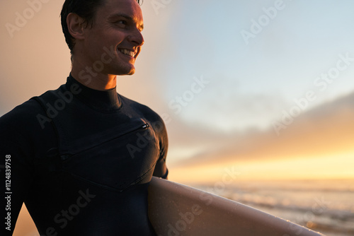 Canvas Print A joyful surfer in a wetsuit smiles while holding a surfboard on the beach at sunset