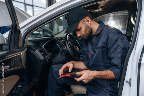 On the seat, with digital tablet. Mechanic working in a car service station