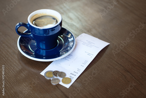 Black coffee in blue mug with bill and money changes on the wooden table in the coffee shop photo