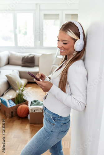 Relaxed break for moving at home, young woman wearing headphones listening to music while packing things from old apartment ready to move and move to new home.