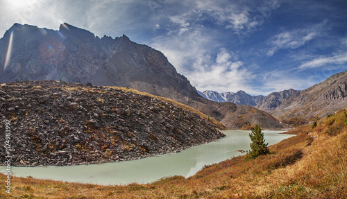 Wild mountain lake, snow-capped peaks, picturesque sky, treeless slopes, sunny day in early fall	