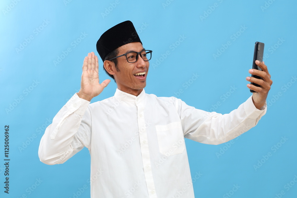 Asian muslim man video call using his phone. Isolated on blue background Asian muslim man video call using his phone. Isolated on blue background