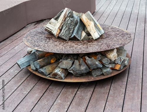 Outdoor fire pit with stacked firewood arranged in a rustic metal design, placed on a wooden deck, for camping, outdoor living, or backyard relaxation themes photo