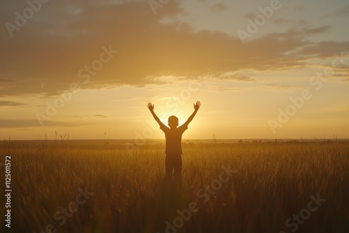 Young boy raising hands at golden sunset in wheat field