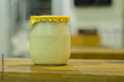 Yogurt in sealed glass jar isolated closeup in blurry background, golden seal color