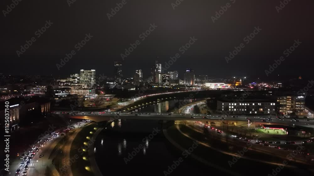 Aerial night view of Vilnius city featuring illuminated buildings, flowing river, and traffic on bridges and streets. Aerial night view of Vilnius city featuring illuminated buildings, flowing river, and traffic on bridges and streets.