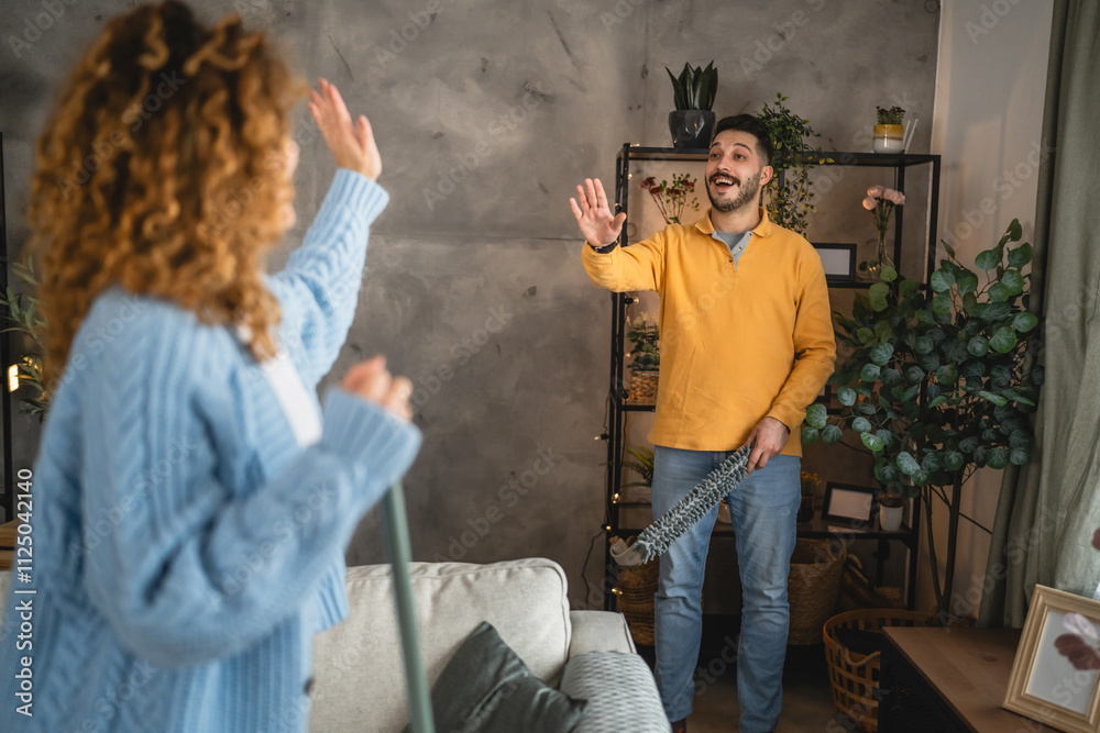 husband dusting shelves in the living room while woman support him husband dusting shelves in the living room while woman support him