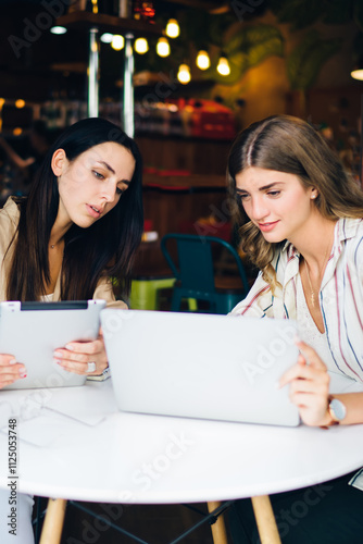 Caucasian freelancers have collaboration meeting for brainstorming in coffee shop with high speed internet connection, skilled female colleagues discussing webinar information watching video on laptop