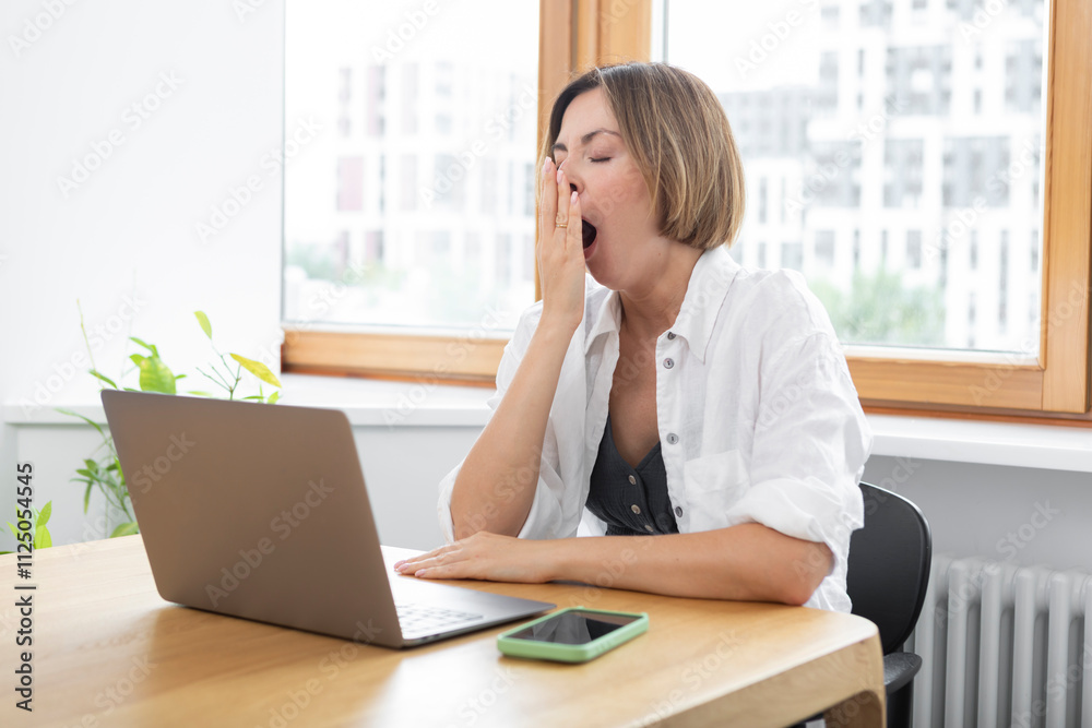 Tired and bored attractive woman sitting at the table and working on laptop in the kitchen at home Tired and bored attractive woman sitting at the table and working on laptop in the kitchen at home