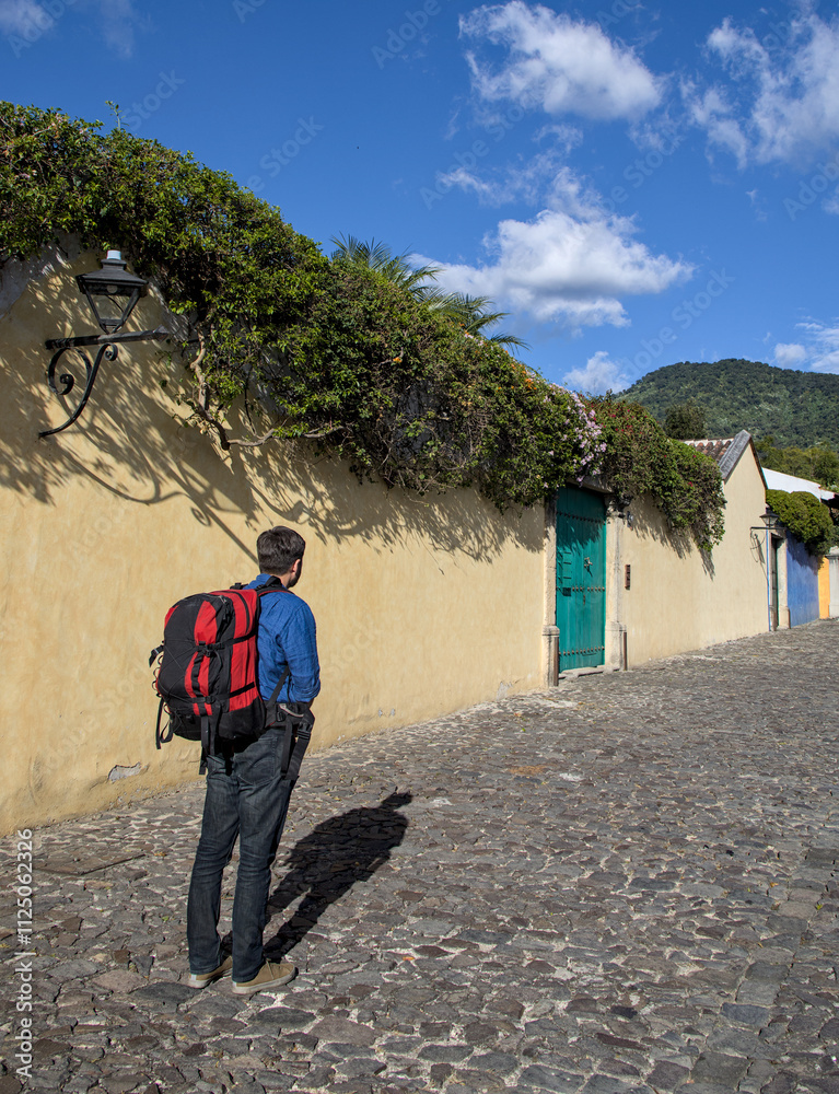 backpacker man with large backpack traveling through antigua guatemala (colonial travel budget tourism destination) colorful street spanish architecture jeans shirt tourist looking up directions phone backpacker man with large backpack traveling through antigua guatemala (colonial travel budget tourism destination) colorful street spanish architecture jeans shirt tourist looking up directions phone