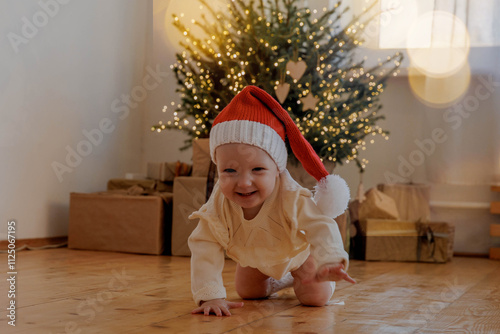 Child in a red Christmas hat crawls under the Christmas tree