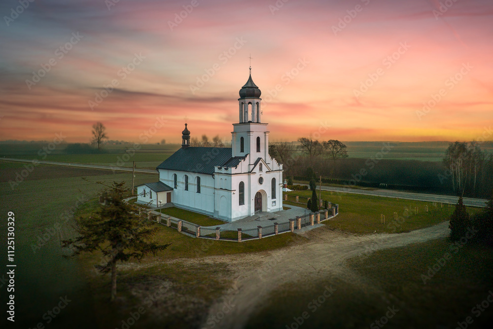 Small, white Catholic church in the light of the setting sun.