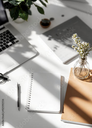 a laptop, notepad, pen and flowers on a desk
