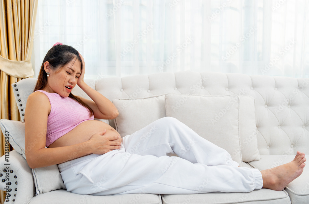 Asian pregnant woman sit on sofa of her house and express like she feel headache also touch her belly. Asian pregnant woman sit on sofa of her house and express like she feel headache also touch her belly.