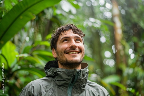 Portrait of a glad man in his 20s wearing a lightweight packable anorak while standing against lush tropical rainforest photo