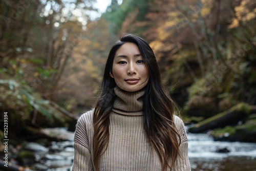 Portrait of a glad asian woman in her 30s wearing a classic turtleneck sweater isolated in tranquil forest stream