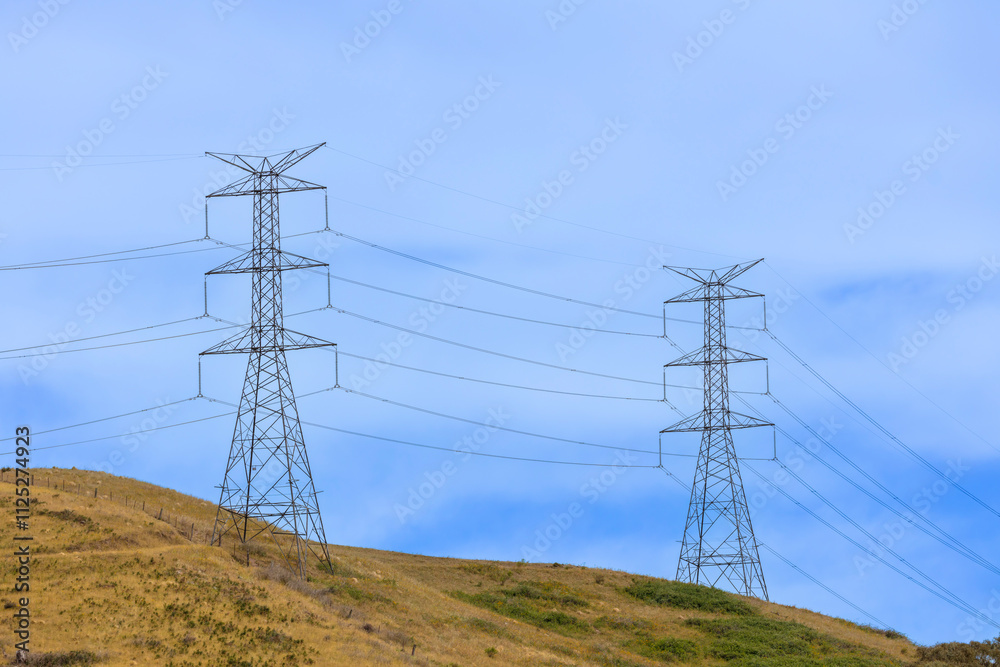 Photograph of a large electricity Transmission Tower on a grassy hill against a bright blue sky in regional Australia.