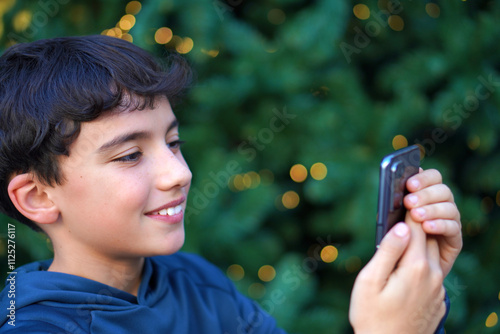 preteen boy making a video call, using his cell phone with a christmas background photo