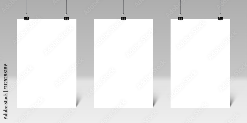 Three blank vertical posters hanging from binder clips on a gray wall create an ideal setting for displaying artwork or designs, enhancing any creative environment or presentation space