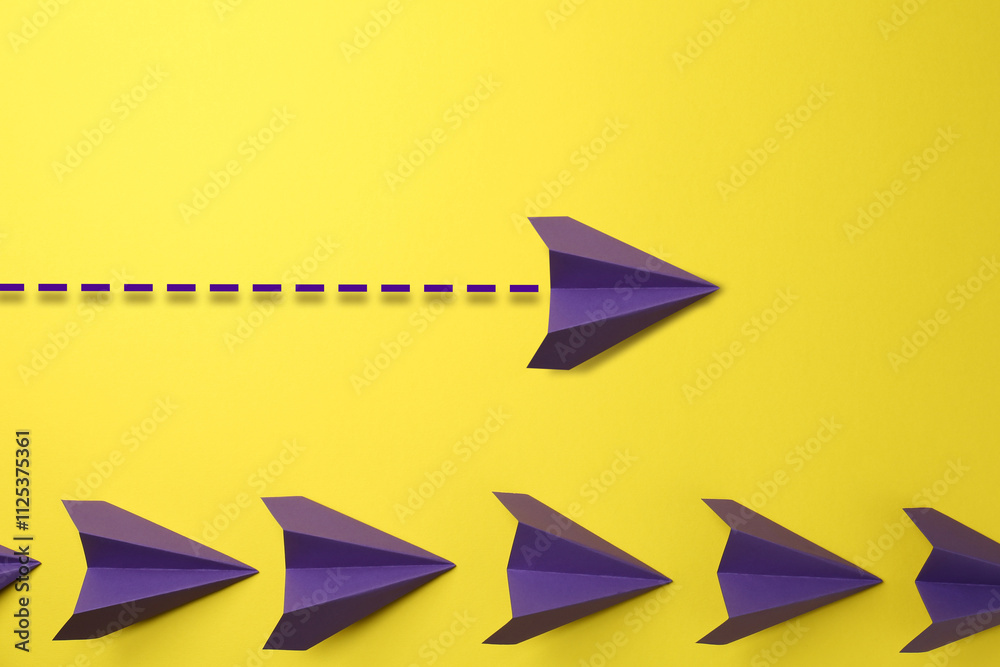 One purple paper plane with flight path over others on yellow background. Dashed line for trajectory One purple paper plane with flight path over others on yellow background. Dashed line for trajectory