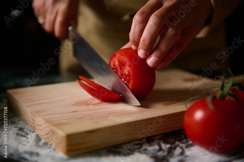 Close-up of hands slicing fresh tomato on wooden cutting board