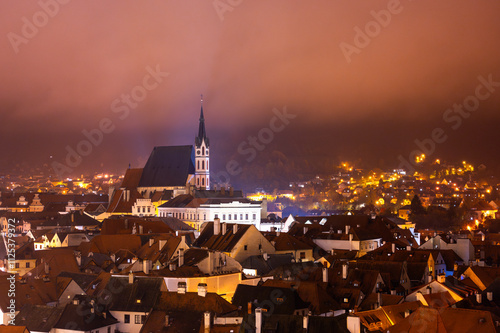 Obraz na płótnie A panoramic night view of Cesky Krumlov, showcasing the rooftops, illuminated buildings, and the Church of St. Vitus beautifully lit up against the dark sky w salonie