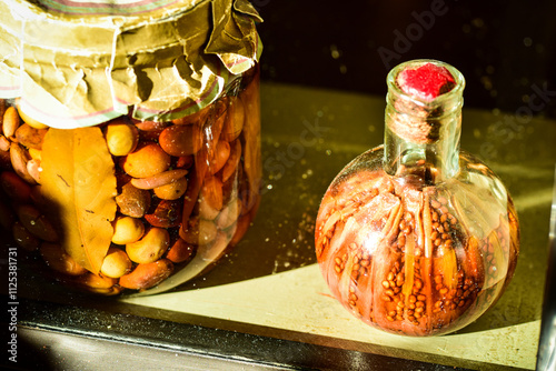 large jar of olives and glass bottle of pickled peppers in sunny window