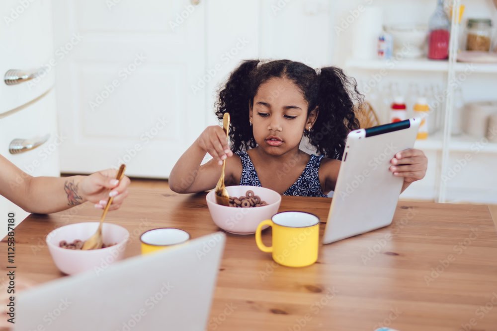 Mother and daughter using gadgets while eating breakfast Mother and daughter using gadgets while eating breakfast