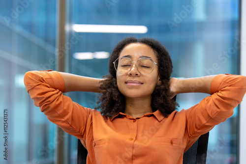 Fotografie A young professional takes a moment to relax at her office desk, leaning back with a smile