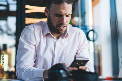 Skilled male freelancer checking received email on smartphone gadget for web browsing during remote job in coworking, Caucasian man sending sms via mobile sitting at desk with modern laptop photo