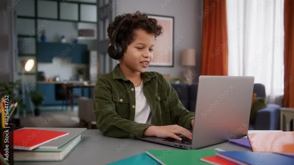 Little happy smile African American boy son child kid gamer gadget addict game playing online internet streaming wearing headphones talking video call e-learning conference class lesson laptop at home