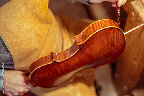 Fotografie Italian violin maker applying varnish on a handcrafted violin in workshop