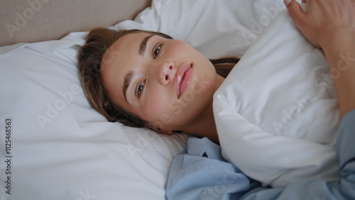 Awaking lady looking camera lying bedroom portrait. Woman covering with blanket