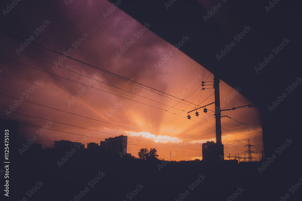 A bright dawn can be seen through the window of a moving train, illuminating the power lines, rails, and silhouette of the city with its rays. A bright dawn can be seen through the window of a moving train, illuminating the power lines, rails, and silhouette of the city with its rays.