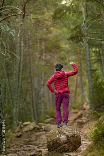 A woman in a red jacket is standing on a rock in a forest