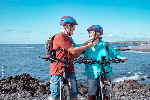 Fototapeta Naklejka Na Ścianę i Meble -  Happy caucasian senior couple wearing helmets riding on the beach with electric bicycles. Authentic elderly retired life concept. Horizon over sea