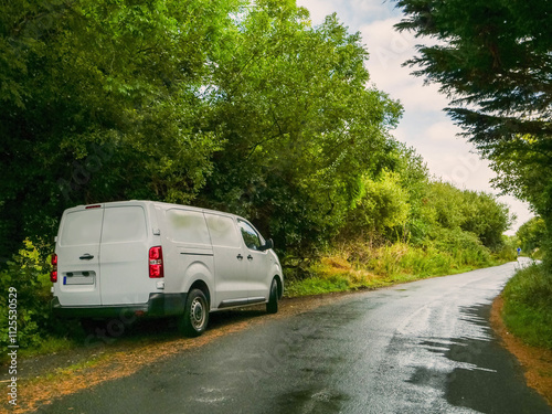 A white medium size van is parked on a small county road in rural area with a red tail light. The road is empty and the sun is shining brightly. Product delivery to remote locations concept. photo