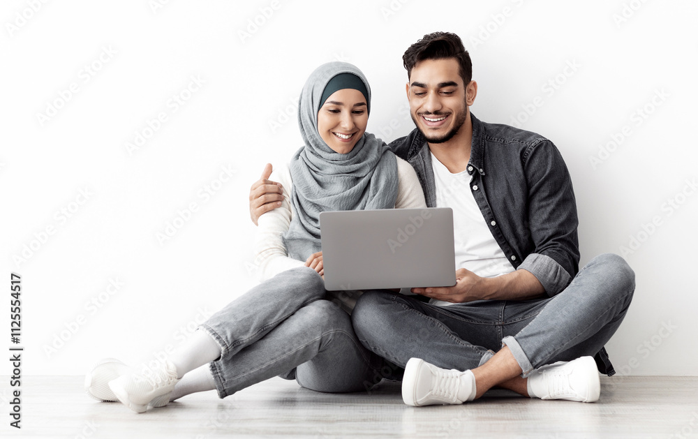 Loving muslim family sitting on floor in new apartment with laptop, buying furniture for house or working on design together, sitting by blank wall, hugging and looking at computer screen, free space Loving muslim family sitting on floor in new apartment with laptop, buying furniture for house or working on design together, sitting by blank wall, hugging and looking at computer screen, free space